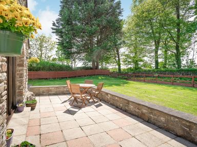 A patio with a round wooden table and four chairs next to a grassy yard with trees and a wooden fence at Highbury in Spittal near Haverfordwest