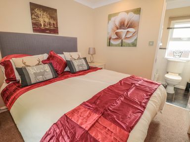 A bedroom with a bed and red bedding next to an ensuite bathroom at Little Gem Lodge in Charlesfield near St Boswells
