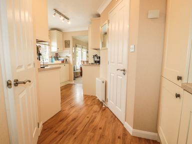 A kitchen with cream cabinets wooden floor and open doors at Little Gem Lodge in Charlesfield near St Boswells