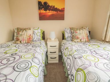 A bedroom with two single beds separated by a bedside table with a lamp and a wall picture at Little Gem Lodge in Charlesfield near St Boswells