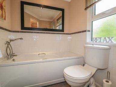 A bathroom with a bathtub a toilet a large mirror and a window with the word relax on the sill at Little Gem Lodge in Charlesfield near St Boswells
