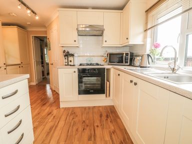 A kitchen with white cabinets a gas stove microwave kettle toaster and a window with blinds at Little Gem Lodge Charlesfield near St Boswells