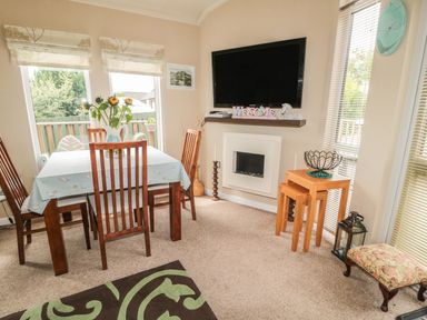 A dining area with a wooden table and chairs a television mounted on the wall a fireplace and side tables at Little Gem Lodge Charlesfield near St Boswells