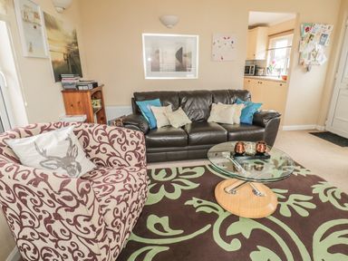 A living room with a patterned armchair a leather sofa and a glass coffee table at Little Gem Lodge Charlesfield near St Boswells