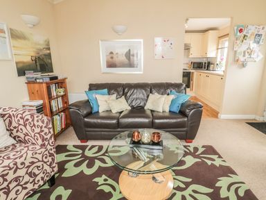 A living room with a dark brown leather sofa and a patterned armchair near a glass coffee table at Little Gem Lodge Charlesfield near St Boswells