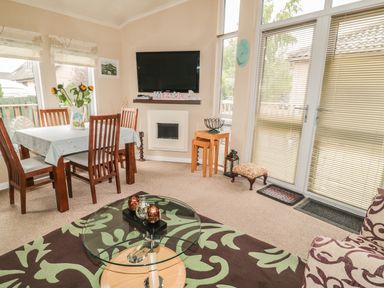 A dining area with a table and chairs next to a television and glass door at Little Gem Lodge in Charlesfield near St Boswells