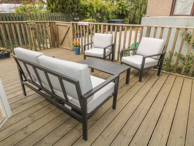 An outdoor wooden deck with metal frame seating and a table at Little Gem Lodge in Charlesfield near St Boswells