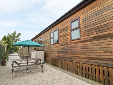An outdoor area with a wooden picnic table and umbrella next to a wooden building at Little Gem Lodge in Charlesfield near St Boswells