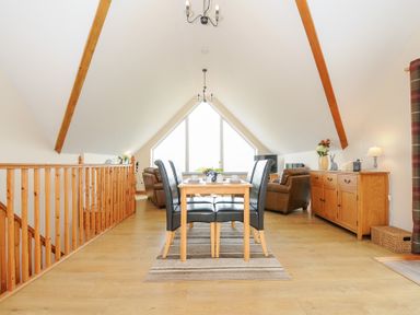 An attic dining and living area with a wooden table and black chairs wooden sideboard brown leather sofas and large triangular window at Treview Launceston