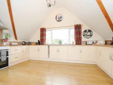 A kitchen with cream cabinets wooden beams and window with red plaid curtains at Treview in Launceston