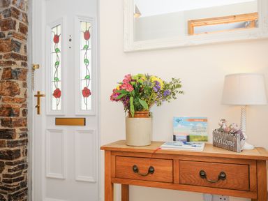 A white front door with stained glass panels next to a wooden table with flowers lamp and welcome sign at Treview in Launceston