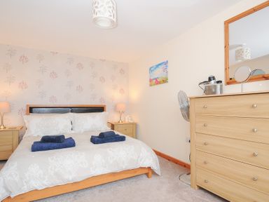 A bedroom with a double bed with towels on it two bedside tables with lamps a chest of drawers a standing fan and a mirror at Treview in Launceston