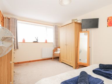 A bedroom with a bed with folded towels a wooden wardrobe a standing mirror a wicker chair a window with curtains and a wall-mounted TV at Treview in Launceston