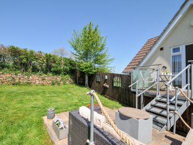 A backyard with green lawn a tree stone wall wooden fence outdoor seating area and house with stairs at Treview in Launceston