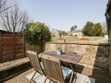 An outdoor patio with a wooden table and four chairs with cushions and a potted plant on the table at The Pound in Trellech near Monmouth
