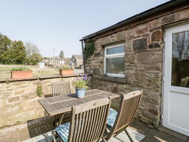An outdoor patio with a wooden table and four chairs with cushions and a potted plant on the table at The Pound in Trellech near Monmouth