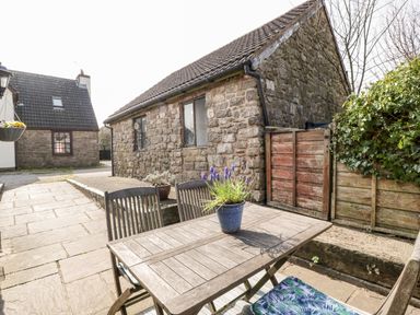 An outdoor patio area with a wooden table and chairs a potted plant on the table stone buildings and a wooden fence at The Pound in Trellech near Monmouth