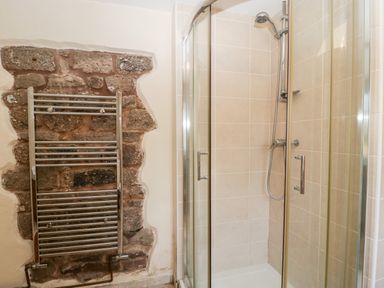 A shower enclosure with glass doors and a showerhead next to a metal towel radiator against a stone wall at The Pound in Trellech near Monmouth