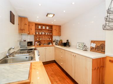A kitchen with wooden cabinets a sink microwave and ceramic mugs on shelves at The Pound in Trellech near Monmouth