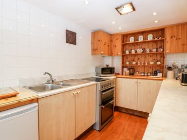 A kitchen with a sink stove microwave wooden cabinets and open shelves holding cups and jars at The Pound in Trellech near Monmouth