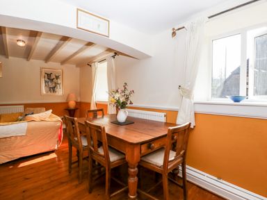 A dining area with a wooden table and chairs next to windows and a sitting area with a sofa at The Pound in Trellech near Monmouth