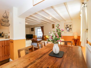A dining room with a wooden table and a vase of flowers overlooking a living room with a television and a lamp at The Pound in Trellech near Monmouth