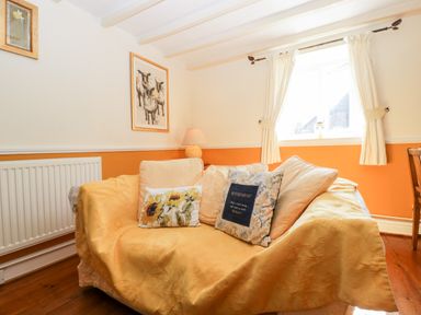 A living room with a sofa covered with yellow fabric and cushions by a window with white curtains at The Pound in Trellech near Monmouth