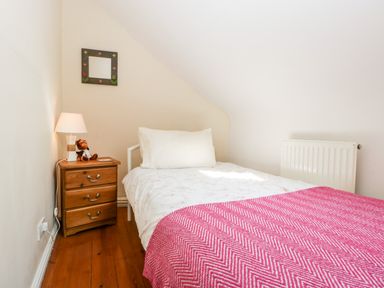 A small bedroom with a single bed a wooden bedside table with a lamp and a stuffed toy a wall mirror and a radiator at The Pound in Trellech near Monmouth