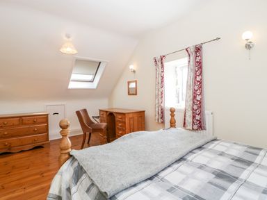 A bedroom with a wooden bed desk chair chest of drawers and window with curtains at The Pound in Trellech near Monmouth