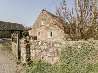 A stone house with three windows and a tiled roof behind a stone wall with plants and a wooden gate at The Pound in Trellech near Monmouth