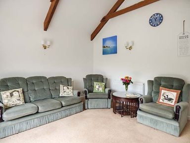 A living room with green upholstered sofa and chairs with pillows and a wooden round table with flowers at Shepherds Rest in Jacobstow near Bude