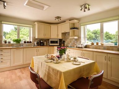 A kitchen with cream cabinets and a table with a yellow tablecloth and tea set at Shepherds Rest in Jacobstow near Bude