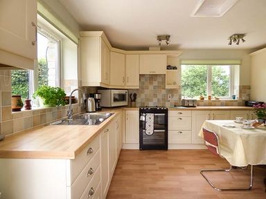 A kitchen with cream cabinets wooden countertops a black oven and a table with chairs at Shepherds Rest in Jacobstow near Bude