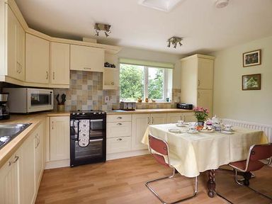 A kitchen with cream cabinets a black oven a table set for tea and two red chairs at Shepherds Rest in Jacobstow near Bude