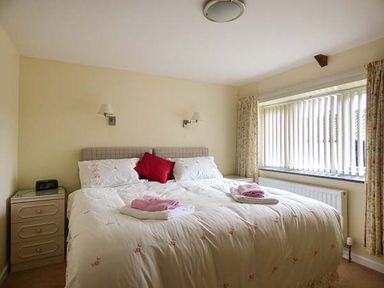 A bedroom with a double bed and bedside tables with lamps near a window with vertical blinds at Shepherds Rest in Jacobstow near Bude