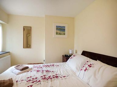 A bedroom with a bed featuring floral bedding a bedside table with a lamp a small wall mirror and a framed picture at Shepherds Rest in Jacobstow near Bude