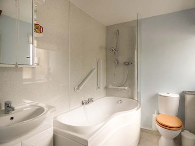 A bathroom with a white bathtub with showerheads a sink and a toilet with a wooden seat at Shepherds Rest in Jacobstow near Bude