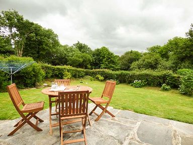 A garden with wooden table and chairs on a stone patio at Shepherds Rest in Jacobstow near Bude