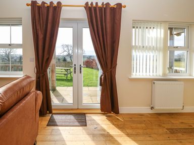 A room with brown curtains on glass doors leading to a garden and a brown sofa at Coquet in Longframlington near Alnwick
