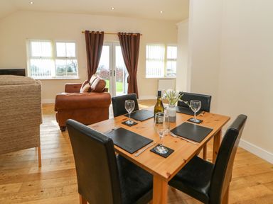 A dining table set with glasses and cutlery next to a living area with sofas and windows at Coquet in Longframlington near Alnwick