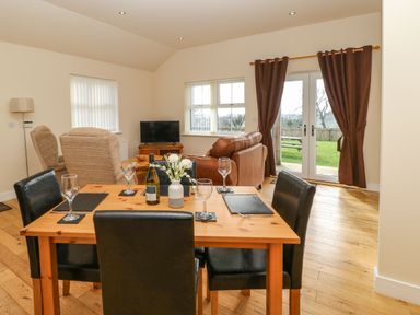 A dining table with chairs and glasses in a living room with sofas a television and doors to a garden at Coquet in Longframlington near Alnwick