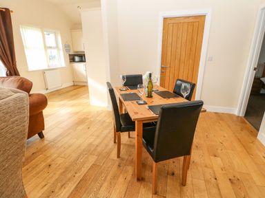 A dining area with a wooden table set with four black chairs glasses and placemats next to a wooden door at Coquet Longframlington near Alnwick