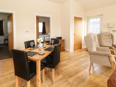 A dining area with a wooden table set for four and two armchairs near a door at Coquet Longframlington near Alnwick