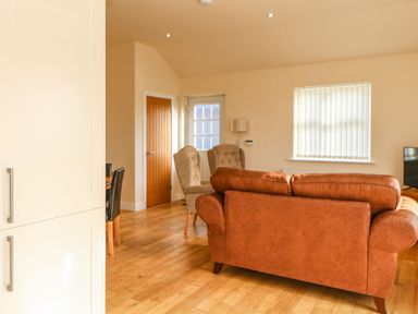 A living room with a brown leather sofa two beige armchairs a wooden floor and a wooden door at Coquet in Longframlington near Alnwick
