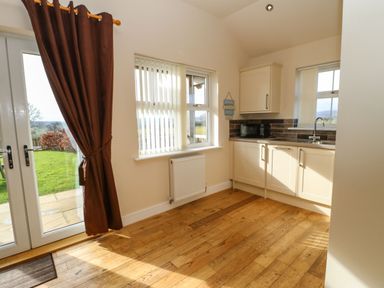 A kitchen area with cream cabinets a microwave a sink windows and a door with brown curtains at Coquet Longframlington near Alnwick