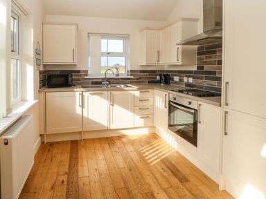 A kitchen with wooden floor white cabinets a window a microwave oven and an electric stove at Coquet in Longframlington near Alnwick