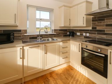 A kitchen with a sink below a window microwave oven kettle and wooden floor at Coquet in Longframlington near Alnwick
