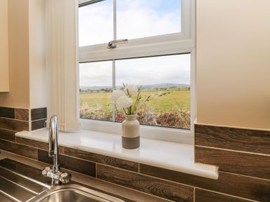 A kitchen sink with a chrome faucet a vase of white flowers on the windowsill and a view of a grassy field through the window at Coquet in Longframlington near Alnwick