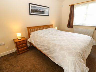A bedroom with a double bed with white bedding two bedside tables with lamps a window with brown curtains and a framed picture on the wall at Coquet in Longframlington near Alnwick