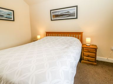 A bedroom with a double bed with white patterned bedding two wooden bedside tables with lamps and framed pictures on the walls at Coquet in Longframlington near Alnwick